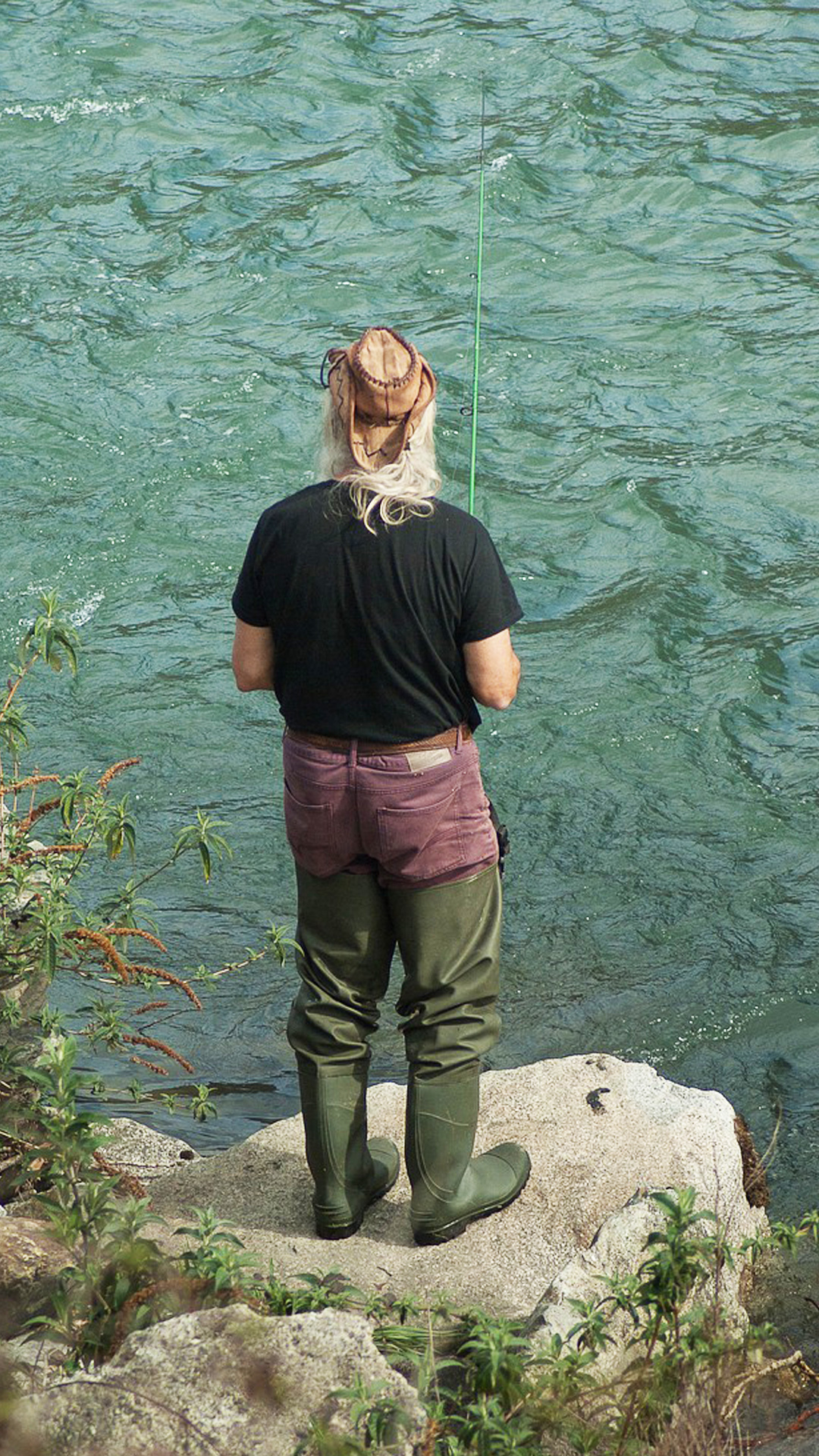 Pêcheur de dos sur un rocher au bord de la rivière.